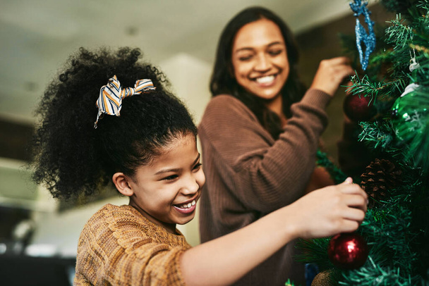 Mère, fille ou collage dans l'arbre de Noël décorant dans la maison ou le salon de la maison pour des vacances festives, célébration ou vacances. Sourire, heureux ou Noël enfant et maman ou enfant et femme dans la décoration légère. - Photo, image
