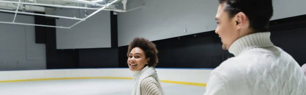 Young african american woman looking at camera near blurred boyfriend on ice rink, banner  - Fotografie, Obrázek