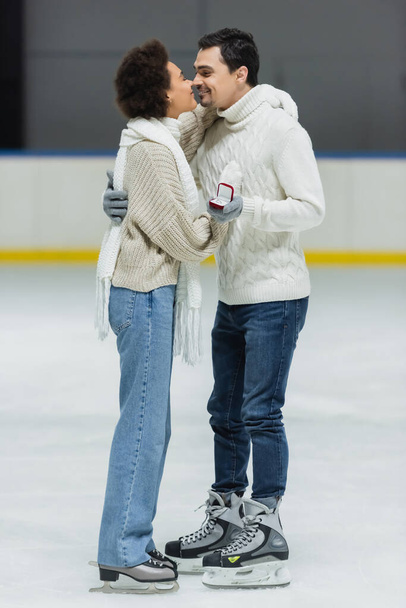 Vista lateral do casal multiétnico com proposta anel beijando na pista de gelo  - Foto, Imagem