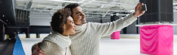 Positive interracial couple taking selfie on smartphone on ice rink, banner  - 写真・画像