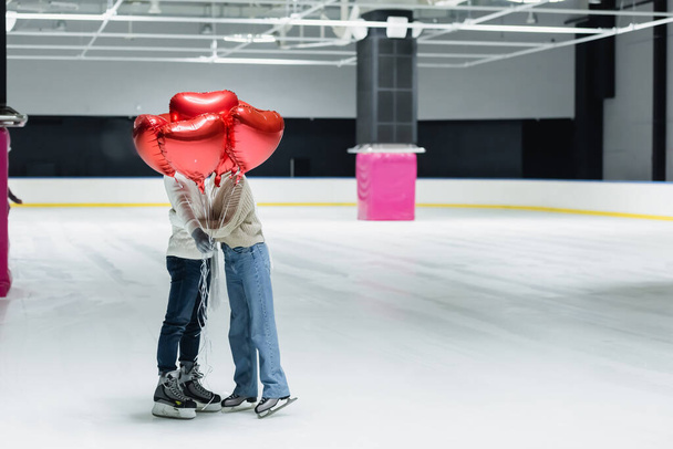 Couple hugging and holding red balloons in shape of heart on ice rink - Foto, afbeelding