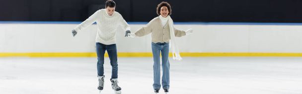 Alegre pareja interracial en guantes calientes patinaje sobre hielo en la pista, pancarta  - Foto, Imagen