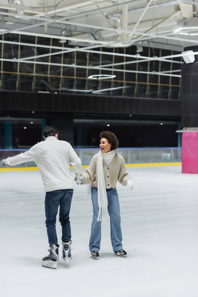 Happy african american woman ice skating with boyfriend on rink  - Photo, Image