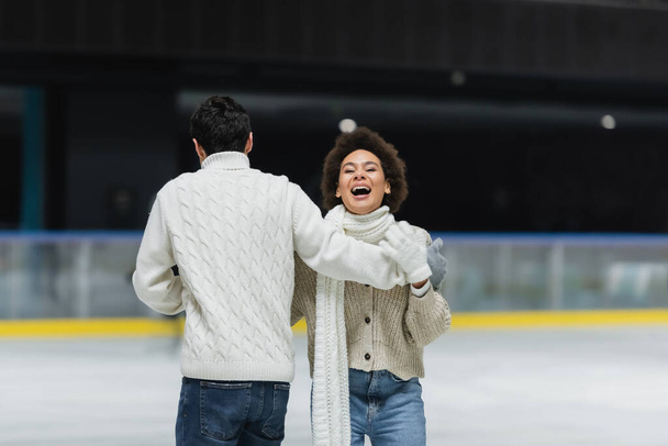 Mujer afroamericana riendo mientras patina sobre hielo con su novio en pista de hielo  - Foto, Imagen