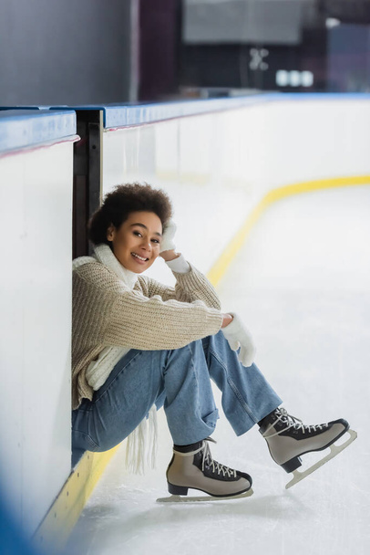 Smiling african american woman in ice skates looking at camera on rink  - Photo, image