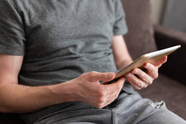 Hombre sentado en un sofá y leyendo algo en una tableta.  - Foto, Imagen