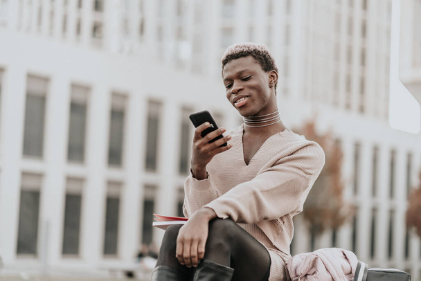 Joven afroamericano chico mirando mensajes en su teléfono inteligente mientras descansa del trabajo duro - Foto, imagen