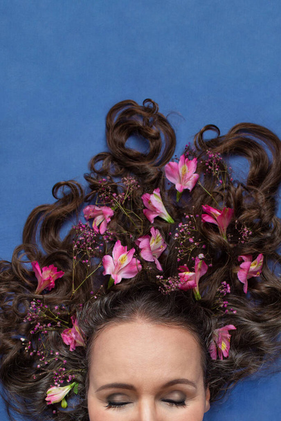 Parte del viso di una donna di mezza età, sdraiata, con gli occhi chiusi e con alcuni fiori nei capelli ricci. - Foto, immagini