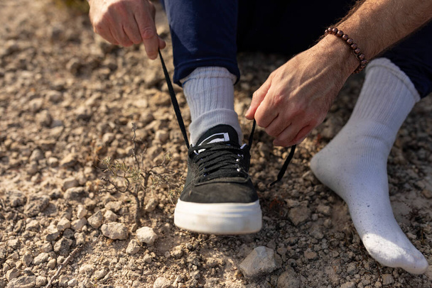 Bir erkek doğadaki yoga seansından sonra ayakkabılarını giymek için ayakkabısının bağcıklarını bağlar. - Fotoğraf, Görsel