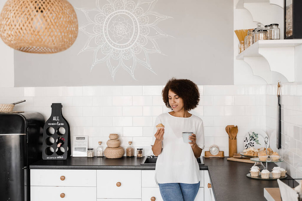 Kodikas aamu afrikkalaiselle amerikkalaiselle tytölle keittiössä kotona. Houkutteleva afrikkalainen nainen kahvia ja kakkua valkoinen keittiö - Valokuva, kuva