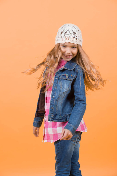 Girl in jeans suit, hat, plaid shirt on orange background. Happy childhood concept. Fashion, style, trend. Beauty, look, hairstyle. Child model smile with long blond hair. - 写真・画像