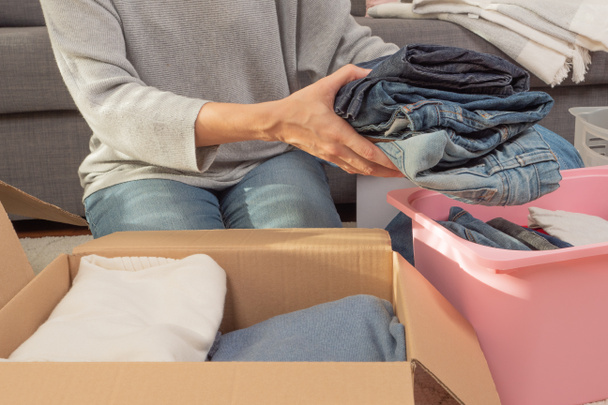 Woman sorting clothes and packing into cardboard box. Donations for charity, help low income families, declutter home, sell online, moving moving into new home, recycling, sustainable living concept. - Fotoğraf, Görsel