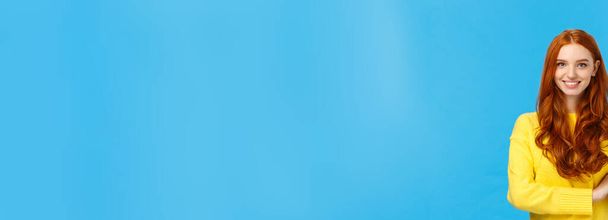 Atractiva mujer pelirroja caucásica confiada y carismática en suéter amarillo, mostrando el número uno, producto de pedido, siendo la primera, sonriendo satisfecha y asertiva, de pie fondo azul
. - Foto, Imagen