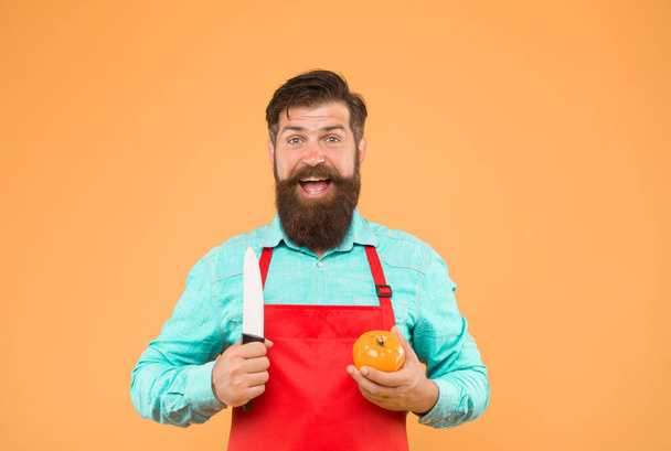 Homem barbudo de avental vermelho com tomate amarelo. cozinhar alimentos saudáveis e frescos. Bonito cozinheiro masculino está a trabalhar. cozinheiro maduro corte vegetal. Um tipo fardado na cozinha. dietas vitamínicas. - Foto, Imagem