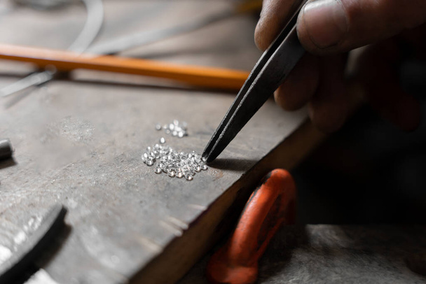 Ein Handwerker Juwelier verwendet die Klemmen, um einige Zirkone aufzuheben, um ein Schmuckstück herzustellen. Konzept des Handwerks - Foto, Bild