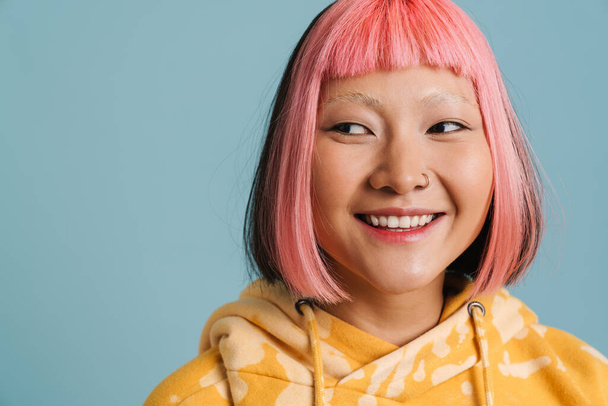 Asian girl with pink hair and piercing laughing while looking aside isolated over blue background - Zdjęcie, obraz