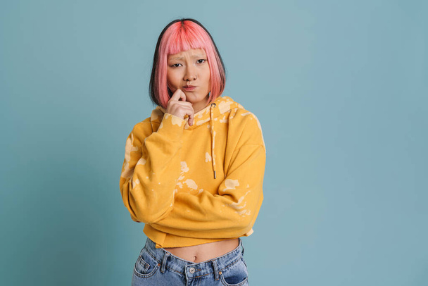 Asian girl with pink hair and piercing frowning while looking at camera isolated over blue background - Photo, Image