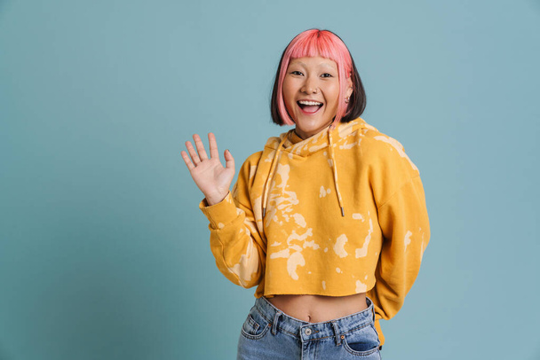 Asian girl with pink hair and piercing laughing while waving hand isolated over blue background - Valokuva, kuva