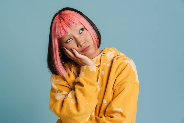 Asian girl with pink hair and piercing frowning while looking aside isolated over blue background - Фото, зображення