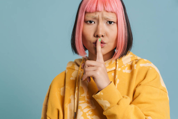 Asiática chica con el pelo rosa y piercing mostrando silencio gesto aislado sobre fondo azul - Foto, Imagen