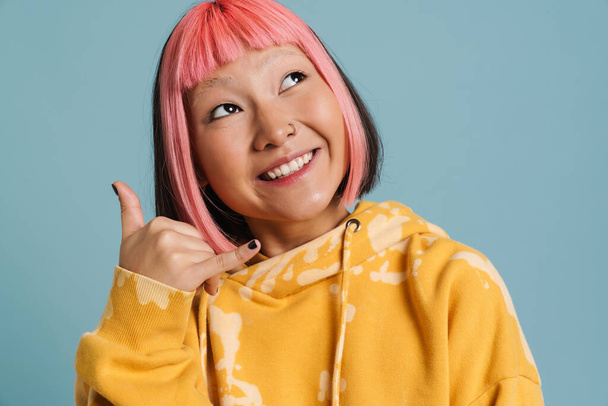 Asian girl with pink hair and piercing making handset gesture isolated over blue background - Foto, Bild