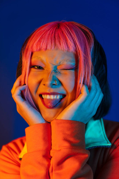 Asian girl with pink hair winking and showing her tongue isolated over blue background - Fotoğraf, Görsel