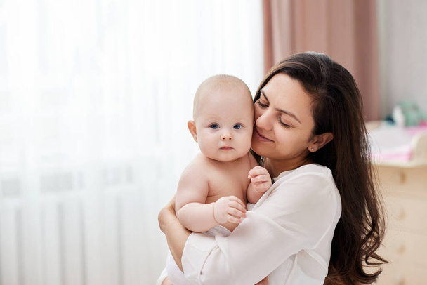 Happy mother holding and hugging adorable newborn baby at home by the window - Foto, Bild