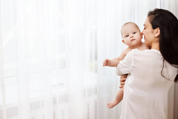 Happy mother holding and hugging adorable newborn baby at home by the window - Foto, Imagen