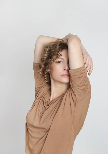 Studio foto van jong vrouwelijk model met beige shirt gemaakt van biologisch katoen. Comfortabele duurzame mode. - Foto, afbeelding