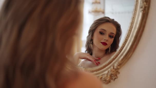 Een modemodel met glanzende make-up in een luxe jurk omhelst zichzelf en ziet er dromerig uit in de spiegel. - Video