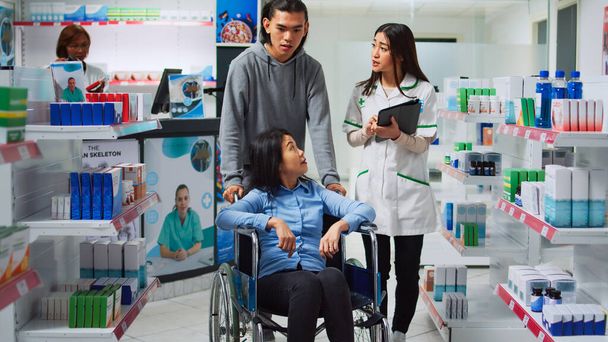 Un employé de pharmacie donne une boîte à pilules à une femme en fauteuil roulant, un homme aidant une personne handicapée. Pharmacien donnant des pilules médicinales au client et au travailleur social en pharmacie. - Photo, image