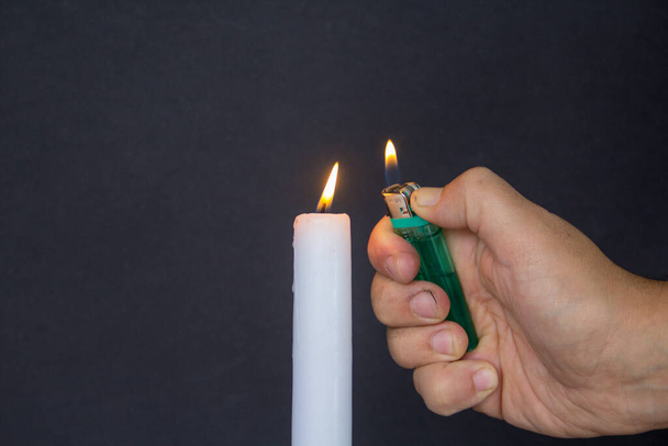 A man's hand holding a lighter while lighting a candle against a black background. - Photo, Image