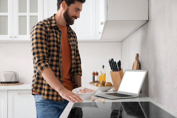 Man making dinner while watching online cooking course via laptop in kitchen - Foto, Bild