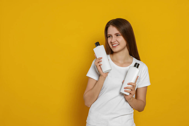 Beautiful young woman holding bottles of shampoo on yellow background. Space for text - Фото, зображення