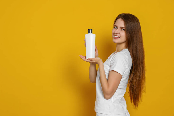 Mooie jonge vrouw met fles shampoo op gele achtergrond. Ruimte voor tekst - Foto, afbeelding