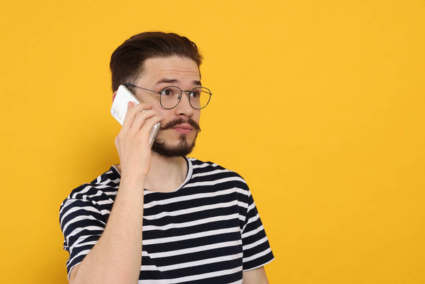 Недовольный мужчина разговаривает по телефону на оранжевом фоне. Пространство для текста - Фото, изображение