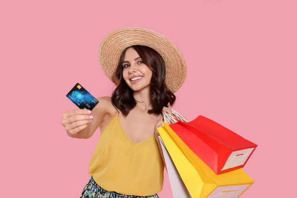 Beautiful young woman with paper shopping bags and credit card on pink background - Foto, Imagem