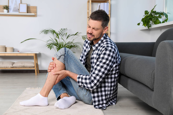 Man rubbing sore leg near sofa at home - 写真・画像