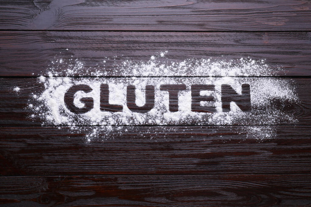 Word Gluten written with flour on dark wooden table, top view - Foto, afbeelding