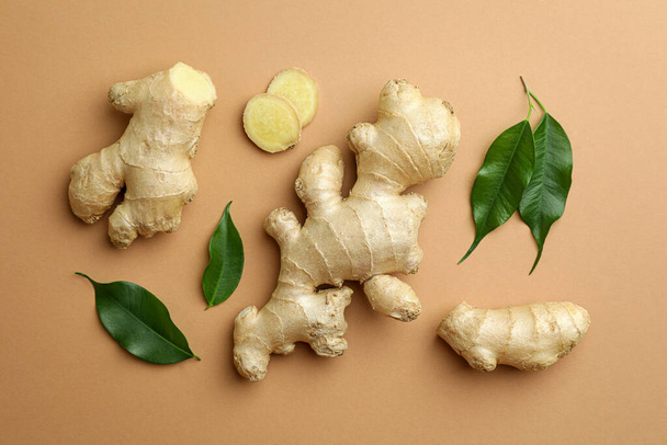 Fresh ginger with green leaves on light pale brown background, flat lay - Φωτογραφία, εικόνα