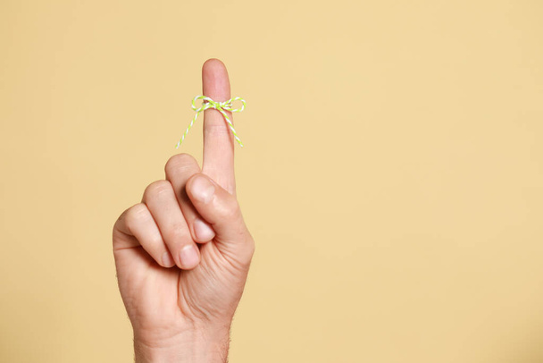 Man showing index finger with tied bow as reminder on beige background, closeup. Space for text - Fotó, kép