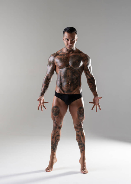 Jonge knappe bodybuilder poseren, atleet toont bodybuilding poseren. hete tattoed man met mooi lichaam toont zijn spieren in de studio - Foto, afbeelding