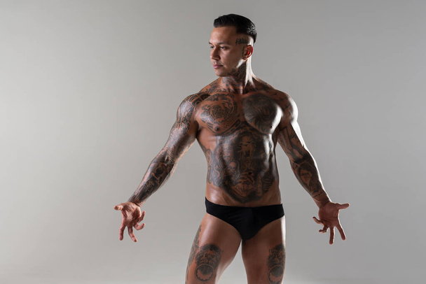 Jonge knappe bodybuilder poseren, atleet toont bodybuilding poseren. hete getatoeëerde man met mooi lichaam toont zijn spieren in de studio - Foto, afbeelding
