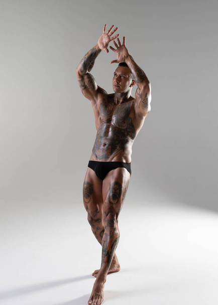 Giovane bel bodybuilder posa, atleta mostra bodybuilding posa. caldo tatuato uomo con bello corpo spettacoli suo muscoli in il studio - Foto, immagini
