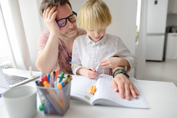 Tired father helping school boy with ADHD do his homework at home. Homeschooling, distance learning, online studying, remote education for kids. Dad involving in raising of child. Parent burnout. - Photo, image