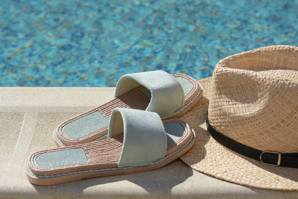 Stylish slippers and straw hat at poolside on sunny day. Beach accessories - Foto, Imagem