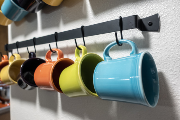 A collection of colorful mugs hanging on black hooks against a white wall - Fotografie, Obrázek