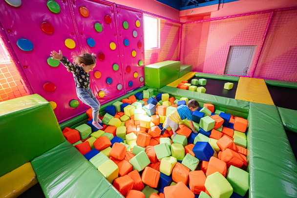 Brother with sister playing at indoor play center playground , jumping in color cubes pool. - Fotó, kép