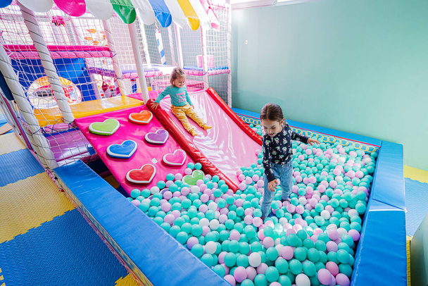 Happy sisters playing at indoor play center playground, color balls in ball pool. - Foto, Imagem