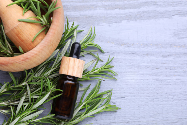 Bottle of rosemary essential oil on wooden table, flat lay. Space for text - Фото, изображение